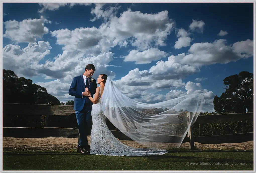 Danelle's veil streams over a rustic fence as Daniel holds her close under big Peel Estate skies
