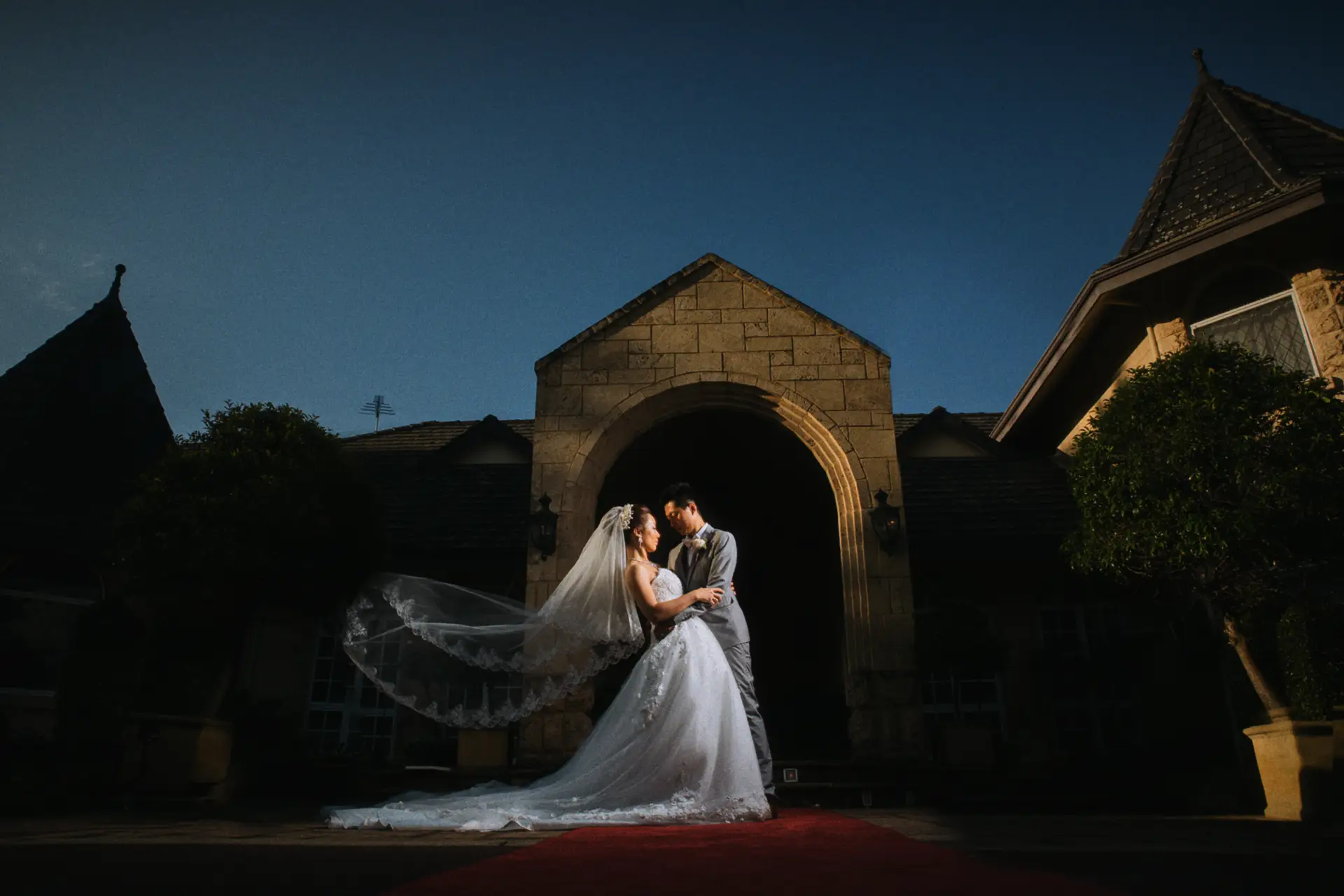 Vivian and Eric embrace beneath the stone archway at Brookleigh, her veil sweeping wide at dusk