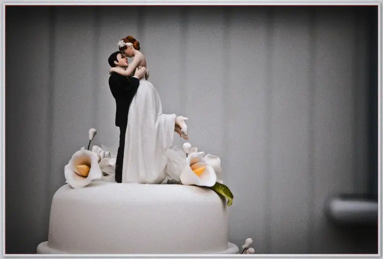 Wedding Photographer - Jaimi and Kevin Mullins-Nutley Close-up of a cake topper couple kissing atop a white wedding cake ringed with sugar calla lilies
