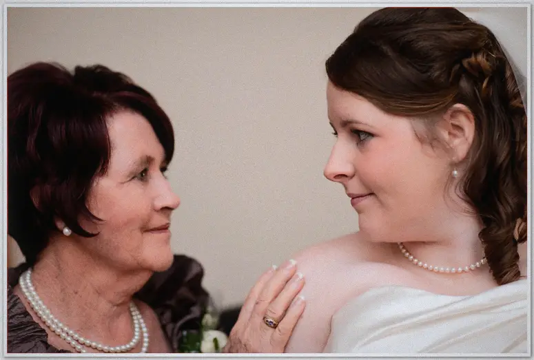Perth Wedding Photographer - Jaimi and Kevin's wedding Mother in pearls rests a hand on her daughter the bride as they share a quiet gaze in a softly lit room