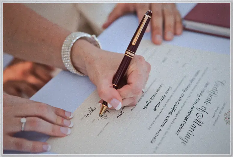 Close-up of Lauren's hand signing the marriage register with a fountain pen and diamante bracelet