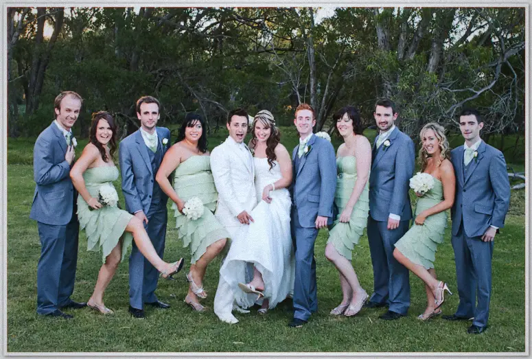 Lauren, Simon and their bridal party lift their legs in a playful mock march on the lawn at dusk