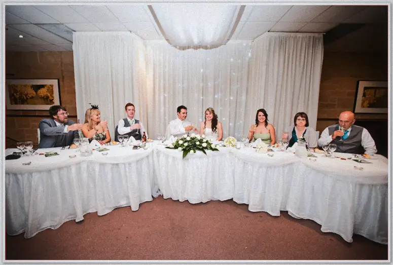 Lauren and Simon raise their glasses at the bridal table beneath a fairy-lit curtain backdrop
