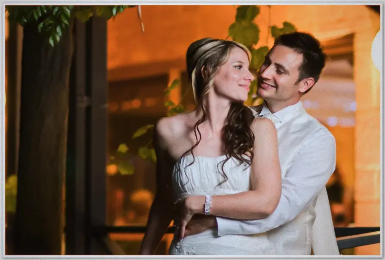 Simon wraps Lauren in a gentle embrace on the deck at night, her gown glowing under canopy lights