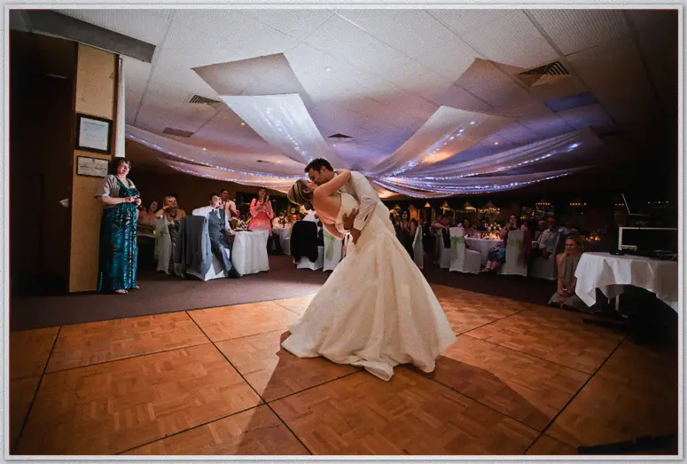 Simon dips and kisses Lauren mid first dance while smiling guests ring the fairy-lit room