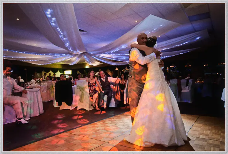 Lauren embraces her father in a warm dance-floor hug under draped fairy lights as guests watch