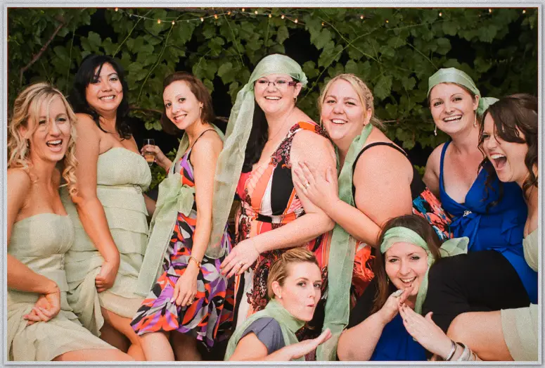A rowdy group of women in colourful dresses and sage scarves ham it up under string lights