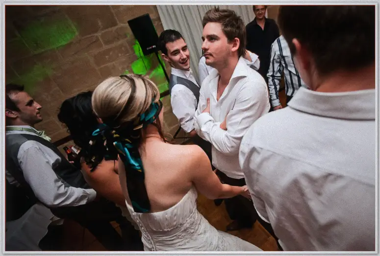Lauren dances with an arms-crossed guest, teal scarf in her hair, green light washing the walls