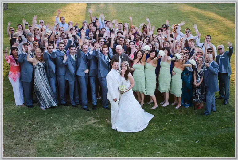 Newlyweds front a jubilant lawn of waving guests during the formal family photo call