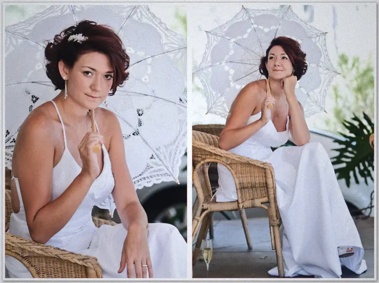 Bride with white lace parasol sits on wicker chair outdoors, champagne flute at her feet