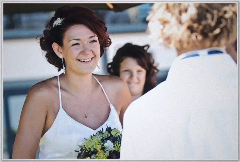 Beaming bride laughs during ceremony, guests blurred behind, bright afternoon light