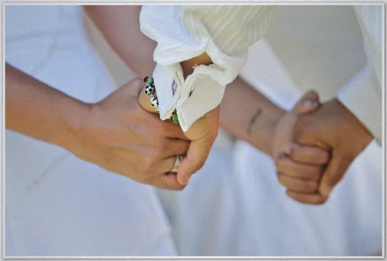 Close-up of the couple holding hands during vows, rings and beaded bracelet in sharp focus