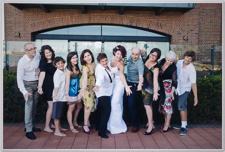 Family group poses with arms outstretched before the brewery's brick archway, brides at centre