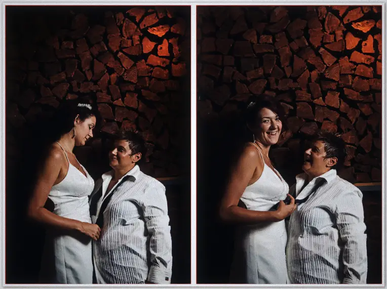Brides nuzzle and burst out laughing beneath a wall of stacked firewood lit warm orange
