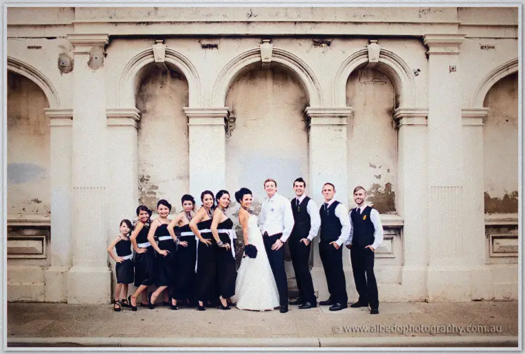 Fremantle Wedding | Charlene and Phil Charlene and Phil flank their bridesmaids and groomsmen beneath the cream arches of a grand Fremantle facade