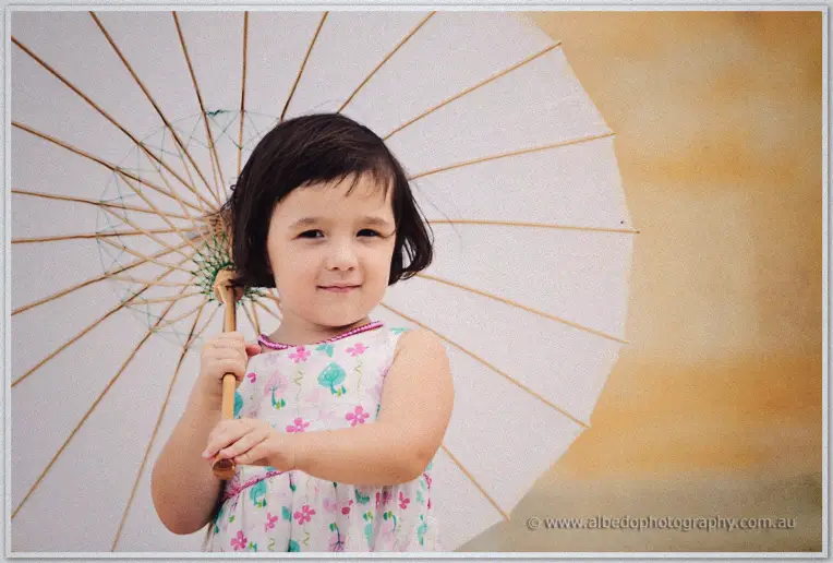 Fremantle Wedding | Charlene and Phil A young flower girl peeks over a white paper parasol against a sun-warmed ochre wall