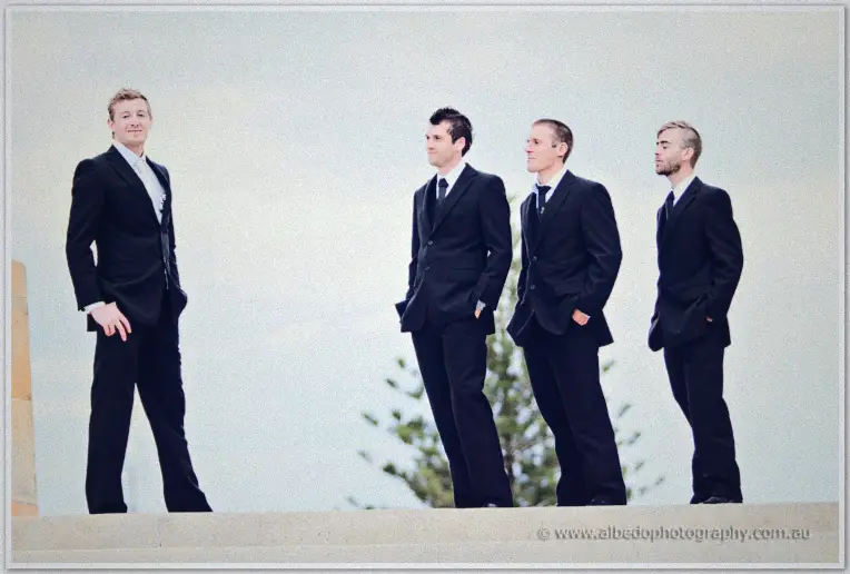 Fremantle Wedding | Charlene and Phil Groomsmen in dark suits stand shoulder to shoulder beneath a hazy coastal sky