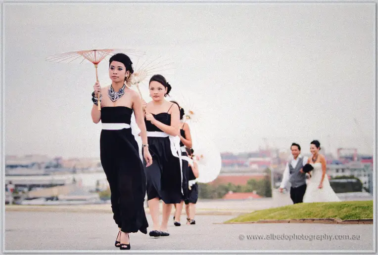 Fremantle Wedding | Charlene and Phil Bridesmaids with paper parasols lead the bride along the esplanade above Fremantle harbour
