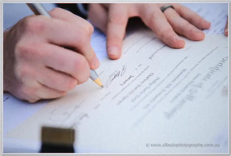 Fremantle Wedding | Charlene and Phil A hand signs the marriage certificate in close-up, pen resting on the official register