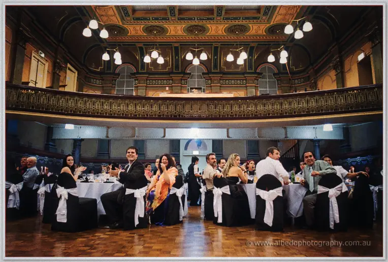 Fremantle Wedding | Charlene and Phil Wedding guests applaud as Phil claps and laughs among candlelit tables in the warm glow of the heritage hall