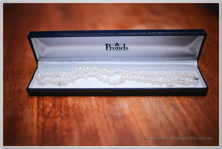 A double strand of white pearls lies in an open navy jewelry box on the polished timber table