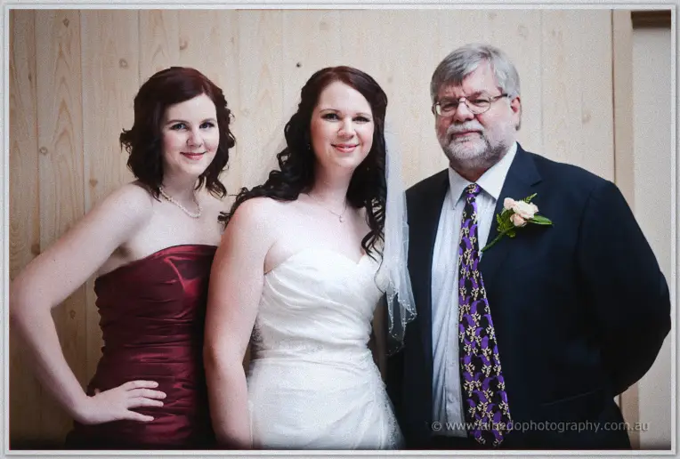 Jenn poses with a bridesmaid in burgundy satin and an older man in a dark suit and patterned purple tie