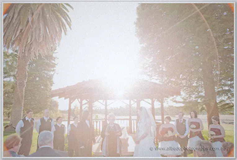 Bright sun floods the gazebo as the celebrant joins Jenn and Lance before their guests by the lake