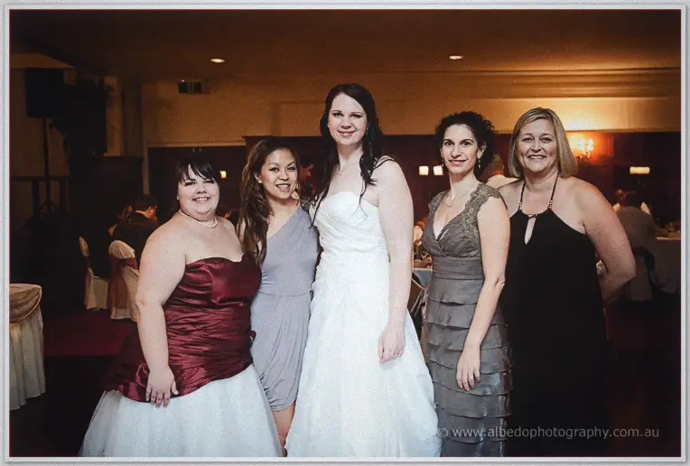 Jenn poses with four friends in mismatched evening gowns in the warmly lit dining room at the reception