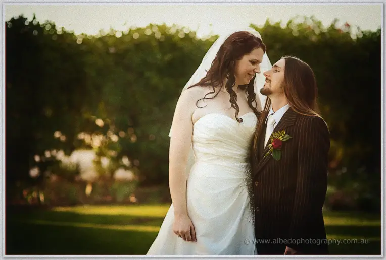 Jenn and Lance lean nose to nose on the lawn, backlit hedges glowing gold behind them