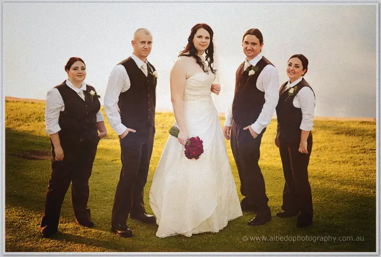 Jenn and four attendants in brown vests pose on the ridge above the water in hazy late light