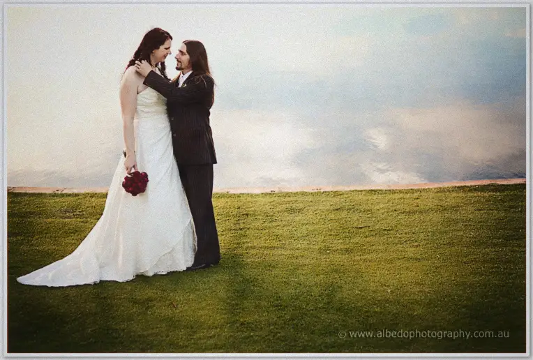 Lance cradles Jenn's neck on the lawn above the still lake, her train sweeping the grass