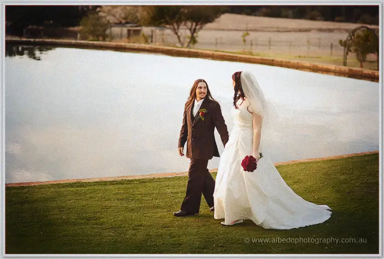 Jenn and Lance stroll hand in hand along the grassy edge of the pond in the late afternoon