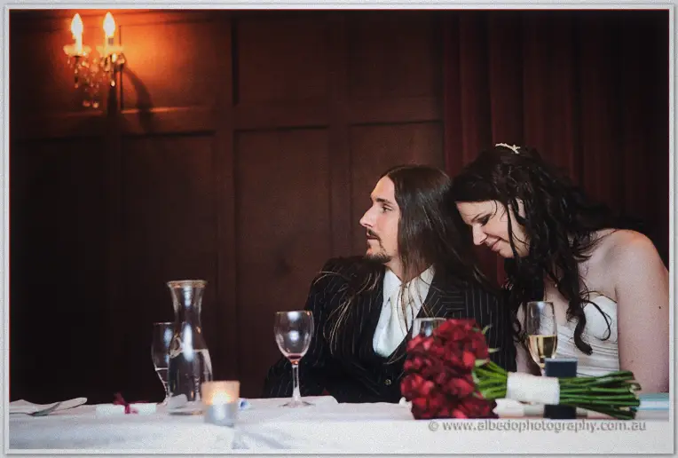 Lance sits at the candlelit head table while Jenn rests her head on his shoulder among roses and glasses