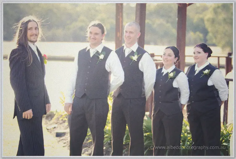 Lance and his four attendants line up by the lake in soft evening light, all in vests and boutonnieres