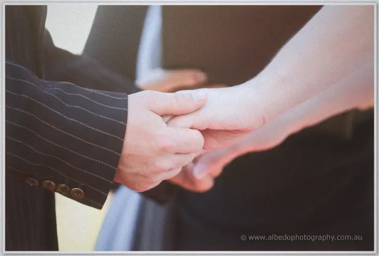 A close view of Lance's hand wrapping around Jenn's as they exchange vows in the afternoon sun