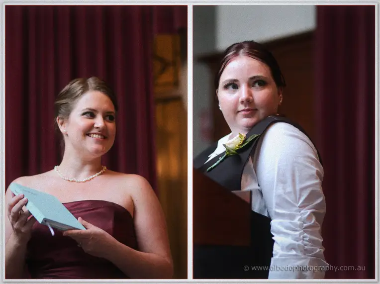 Bridesmaids in burgundy gowns hold a reading book and glance back beneath deep red ceremony curtains