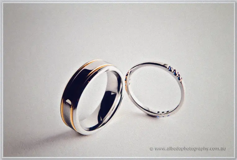 Two wedding rings, a wide polished band beside a slim gem-set ring, on a pale surface