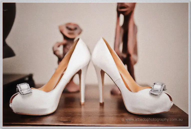 Emily's white peep-toe heels with crystal buckles wait on a polished timber table