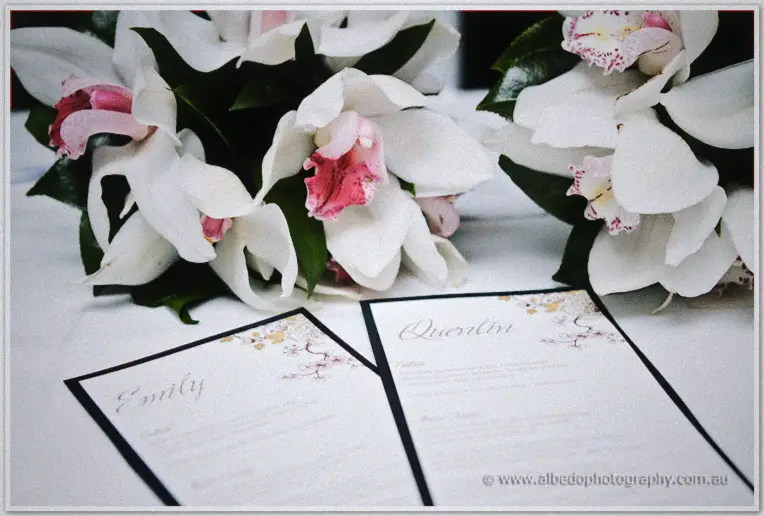 Place cards for Emily and Quentin rest beside white orchid bouquets on a white tablecloth