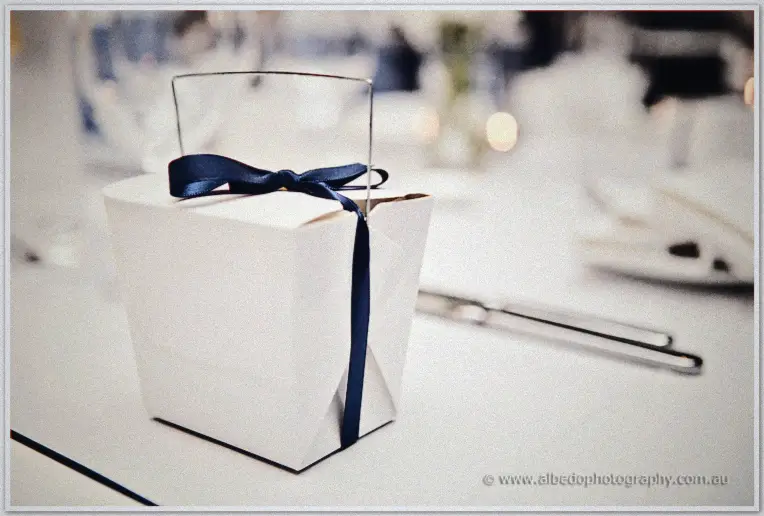 A white favour box tied with navy ribbon sits on the reception table amid fairy lights