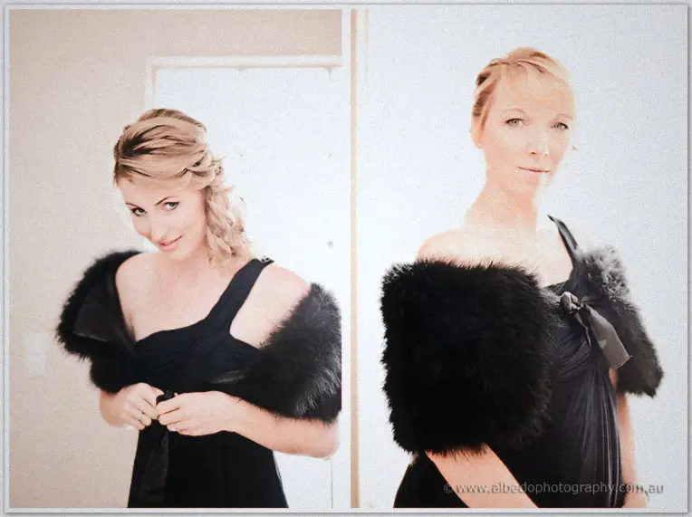 Two bridesmaids in black dresses with feathered shrugs prepare in soft morning light