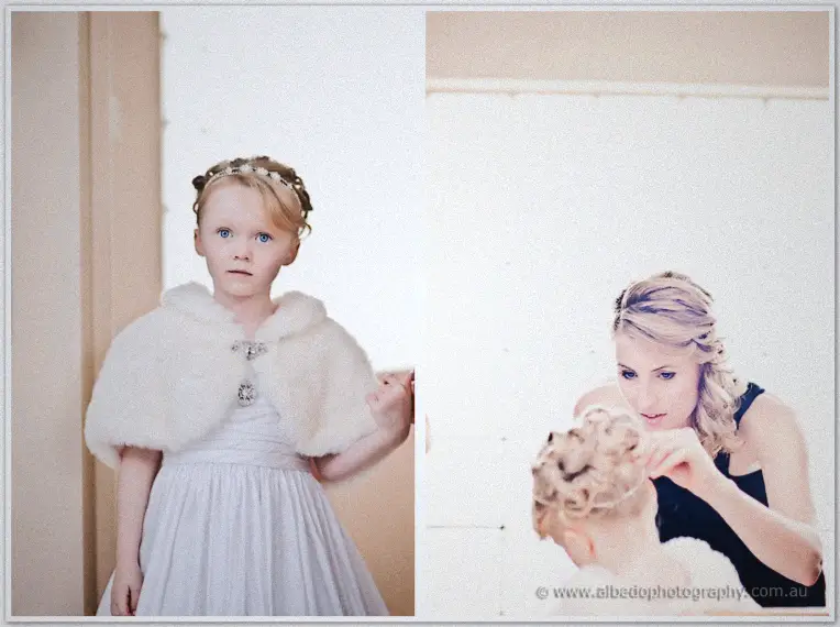 The flower girl in a white dress and furry cape watches as a curling iron is styled near her hair