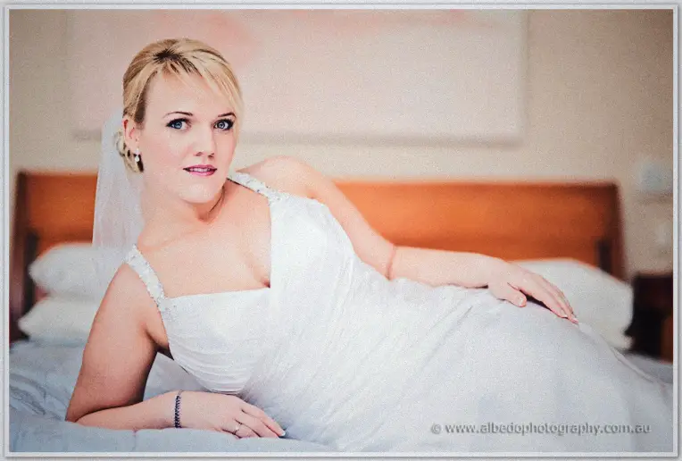 Emily reclines on a bed in her wedding dress and veil, soft light in a bright bedroom