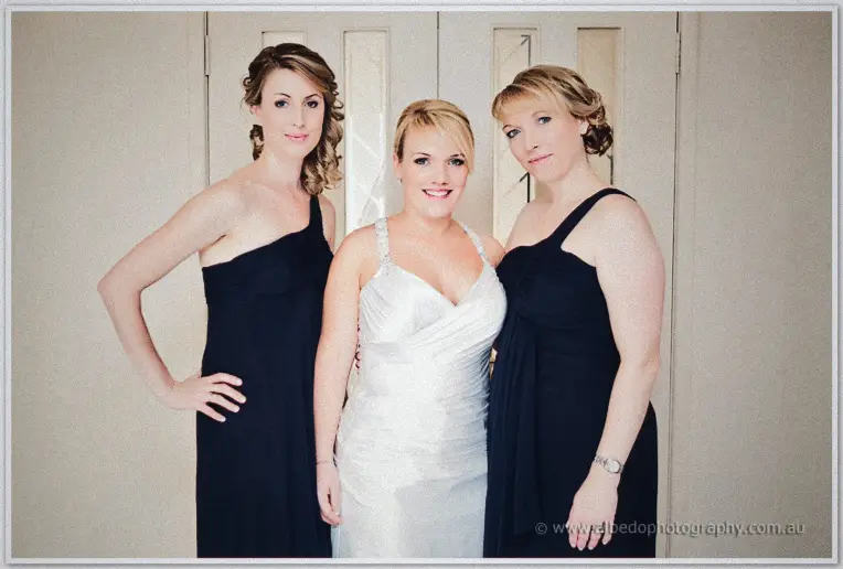 Emily stands between her two bridesmaids in navy gowns for a group portrait indoors