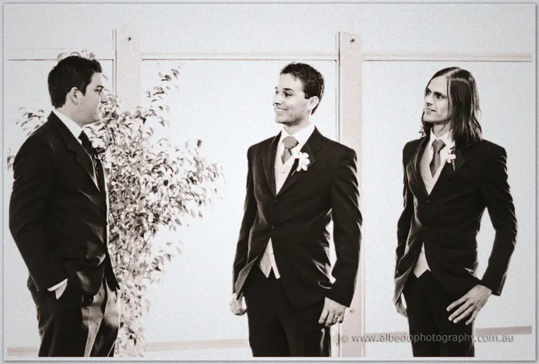 Quentin grins with his groomsmen as they wait in dark suits at the marquee ceremony