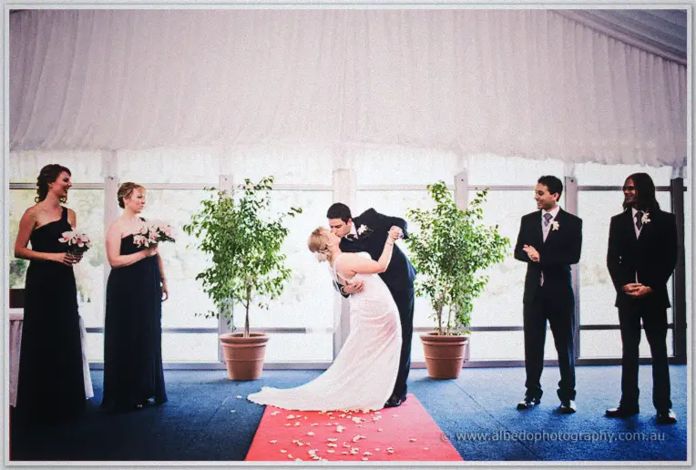 Quentin dips Emily for a kiss on a petal-strewn aisle before their bridal party