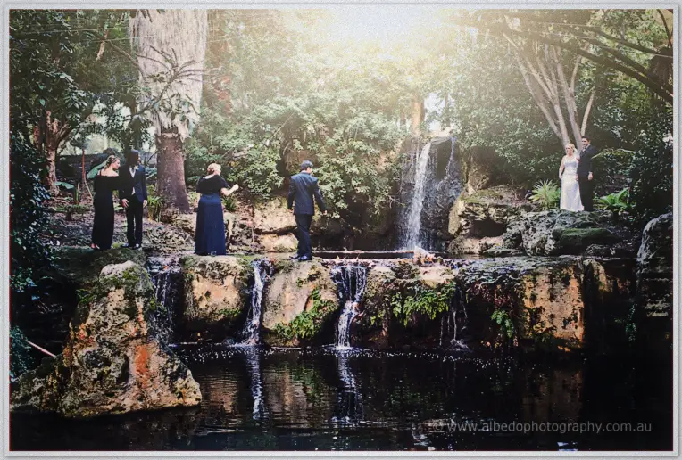 The bridal party poses on mossy rocks around a cascading waterfall in golden light