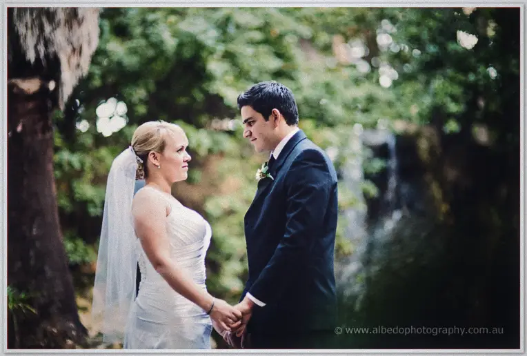 The newlyweds hold hands by a waterfall and pond in a lush Perth garden