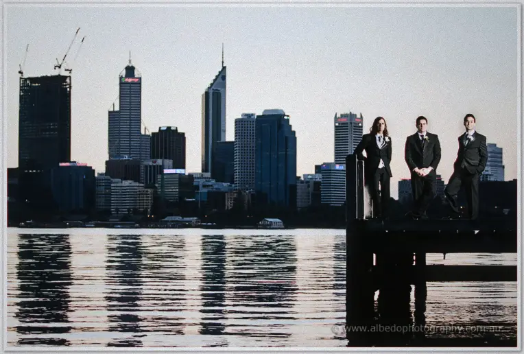 Groomsmen line a jetty post against the Perth skyline reflected in the river at dusk