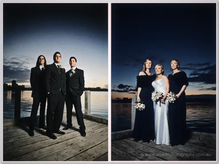 Groomsmen and bridesmaids pose apart on the jetty planks under a deepening twilight sky
